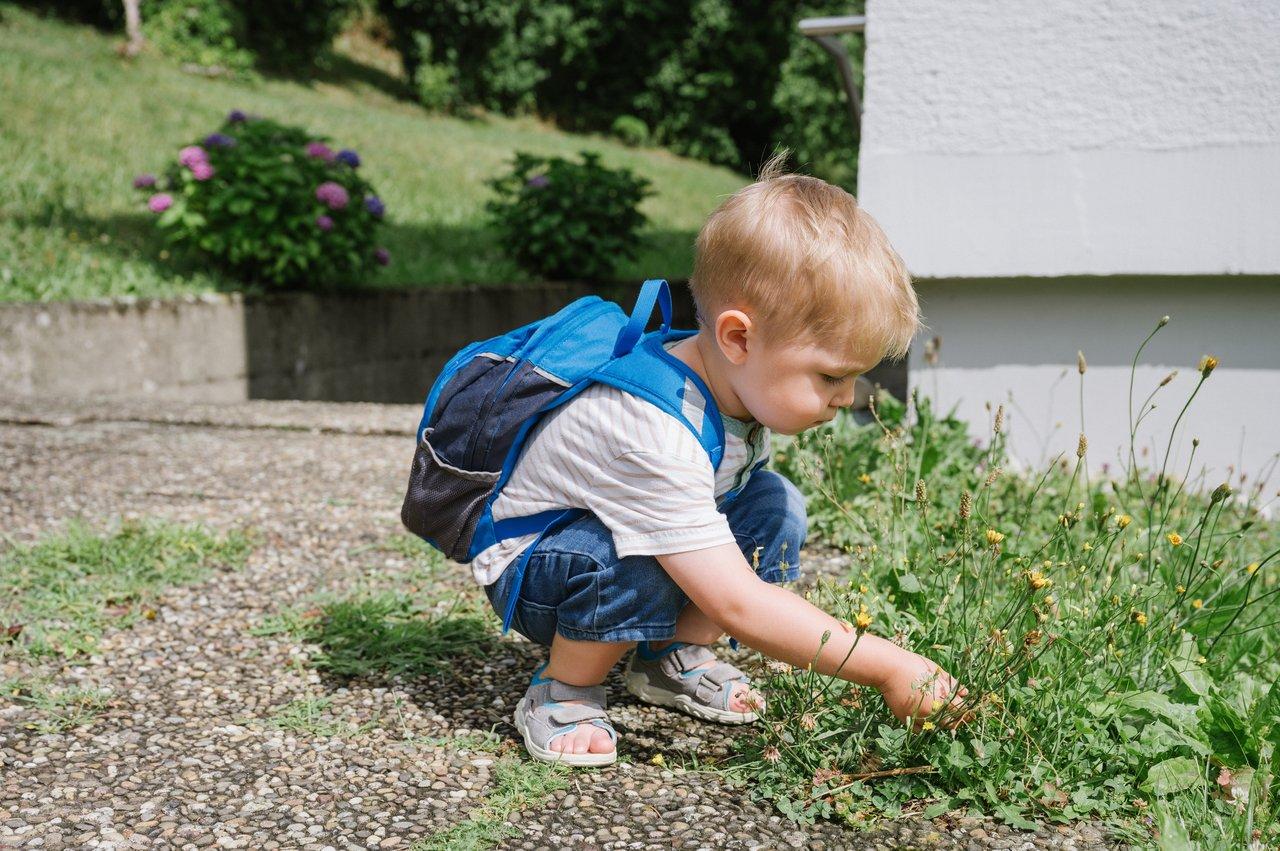 Enfant jouant librement avec des matériaux naturels dans un jardin, favorisant l'estime de soi chez les jeunes.